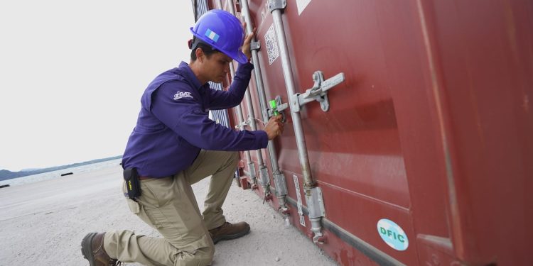 Trabajador con casco y uniforme revisa el mecanismo de cierre de un contenedor de carga.
